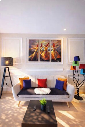A modern living room with a sofa, colorful cushions, a coffee table with remotes, a floor lamp, and a painting on the wall. - Beautiful apartment in downtown Marrakesh—3 outdoor pools, a golf course, and a terrace (Marrakech)