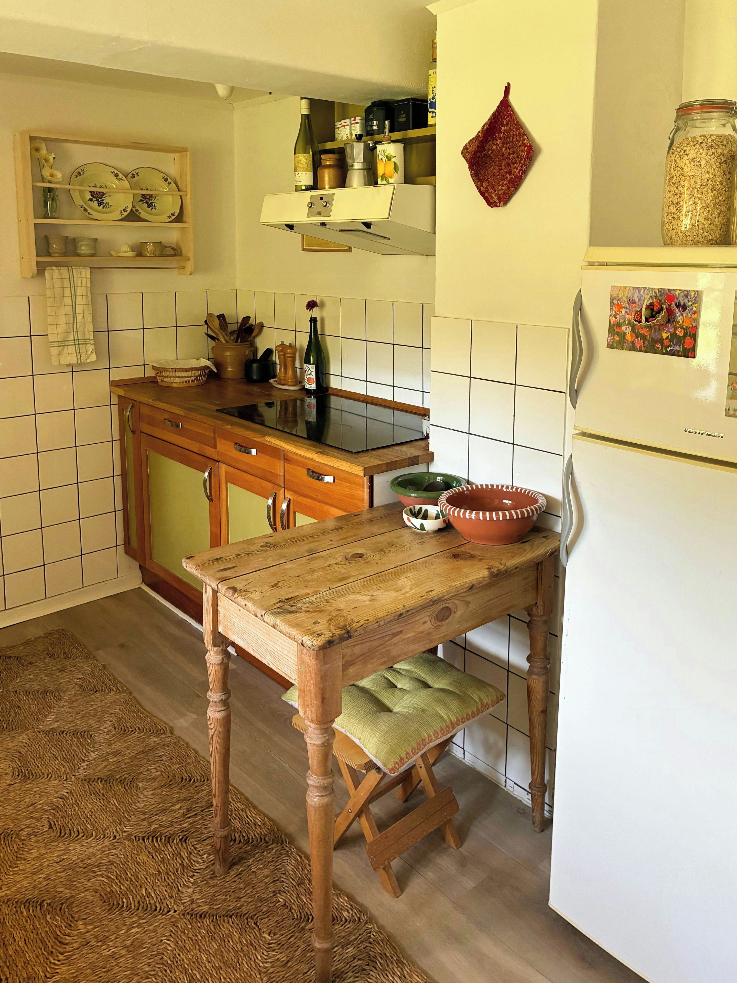 Eine Küche mit einem Holztisch, einer grünen Schüssel und einem weißen Kühlschrank.