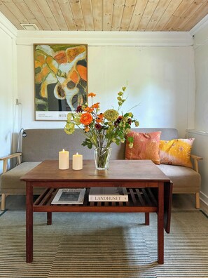 Un salon avec une table basse en bois, un vase de fleurs, une bougie allumée et un canapé avec des coussins.
