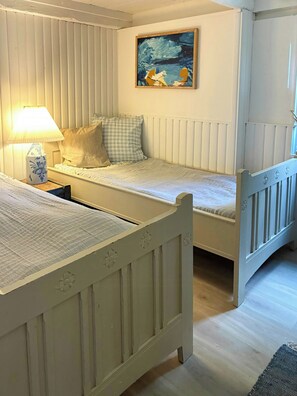 A room with two single beds, a nightstand with a lamp, a painting on the wall, and a window with blinds. - Country house with wild garden and field views (Vig)