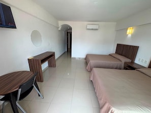 A hotel room with two beds, a desk, a chair, a round mirror, an air conditioning unit, and a television. - Hoteles Guru Xi Mar (Acapulco de Juárez)