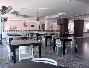A hotel lobby with multiple dining tables and chairs, a reception desk, and a television screen. - Hoteles Guru Xi Mar (Acapulco de Juárez)