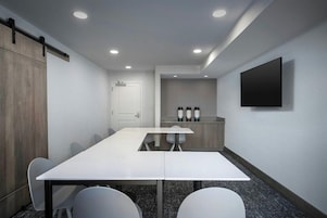 Un salón de conferencias con una mesa larga, sillas, una televisión y una puerta.