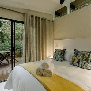 A bedroom with a large bed, a view of greenery outside, and a wooden deck area. - L Auberge Country Hideaway (Gqeberha)