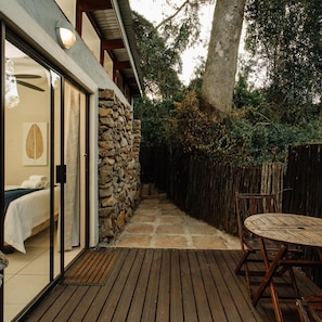 A wooden deck with a stone wall, a bed with white bedding, and a dining table with chairs. - L Auberge Country Hideaway (Gqeberha)