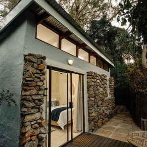 A modern house with a stone exterior, a bedroom with a bed and curtains, and a wooden deck. - L Auberge Country Hideaway (Gqeberha)