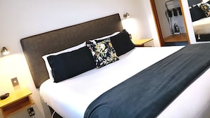 A neatly made bed with a dark headboard, white bedding, and two decorative pillows. - Asure Dunedin Academy Court Motels (Dunedin)