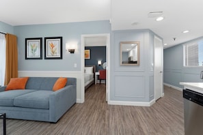 Ett modernt vardagsrum med en grå soffa, en matplats med ett vitt bord och ett kök med diskmaskin.