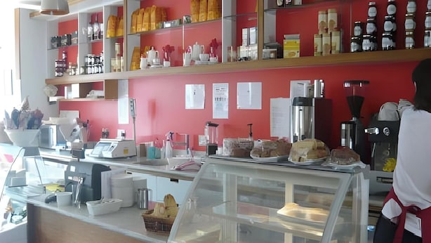 A bakery counter with various baked goods on display, a coffee machine, and a counter with a cash register.