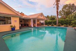 Un patio trasero con piscina, un área de patio techada y una casa con chimenea visible.