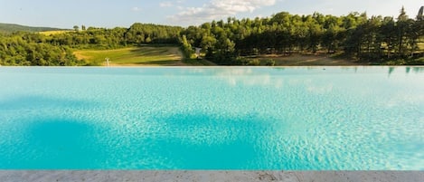 A clear blue infinity pool with a view of a green landscape and trees.