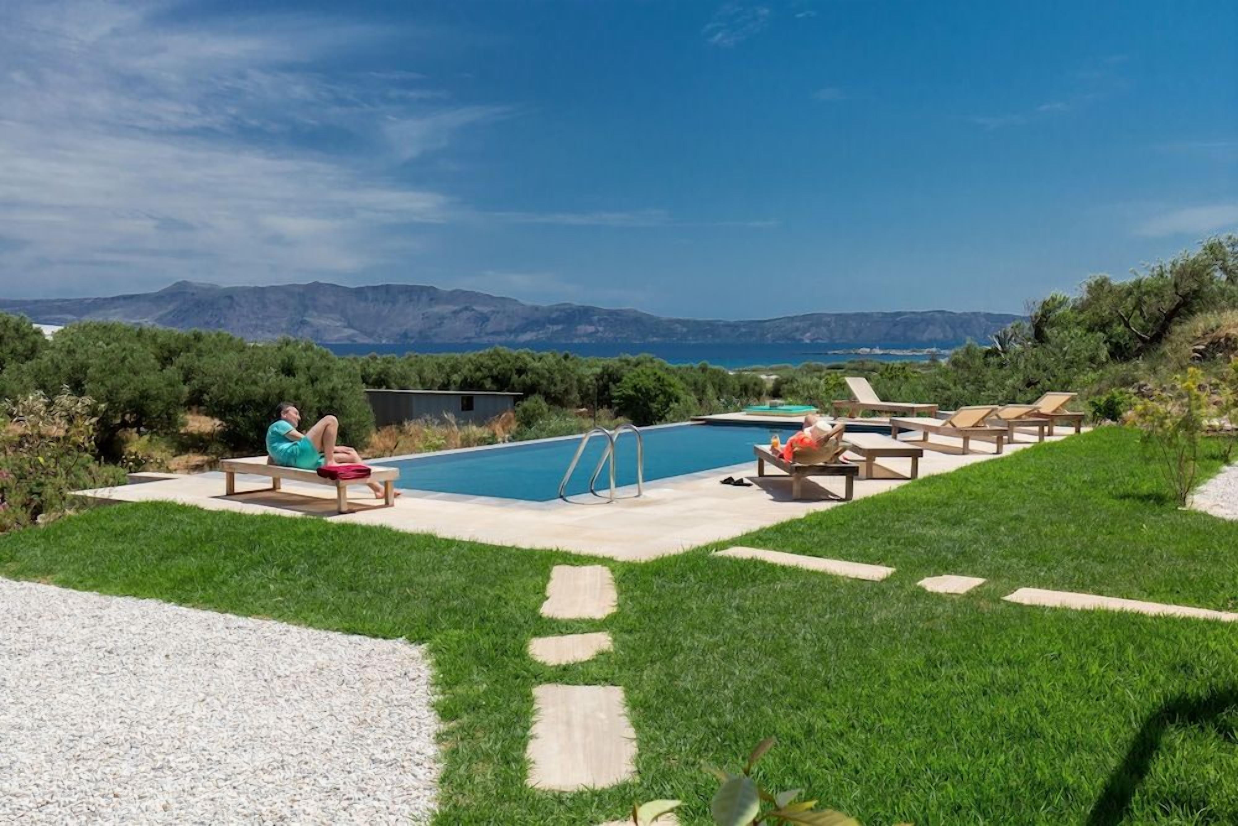 Piscina com espreguiçadeiras e vista para o mar e montanhas.