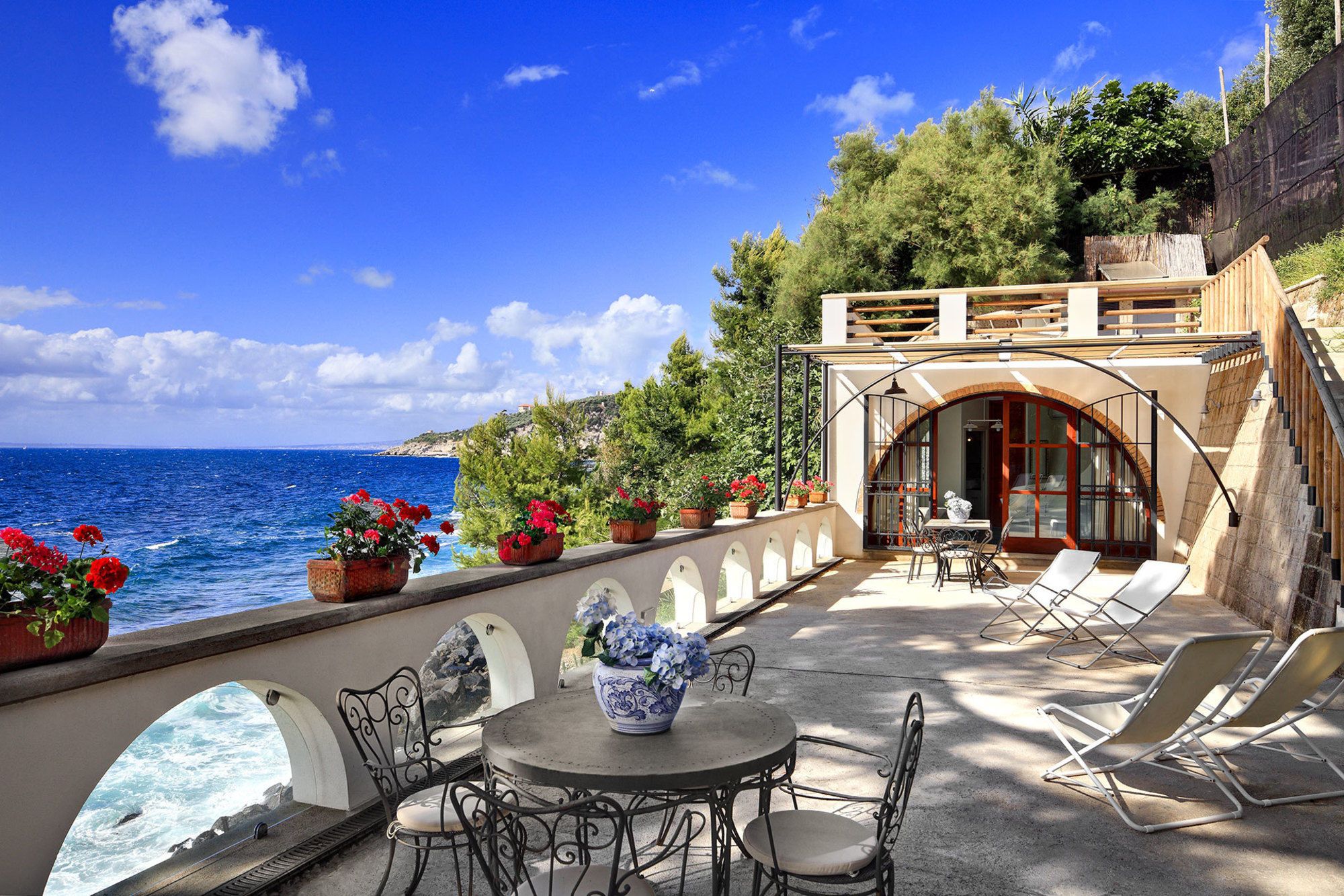 Una terrazza con vista sul mare, arredi da esterno e piante in vaso.