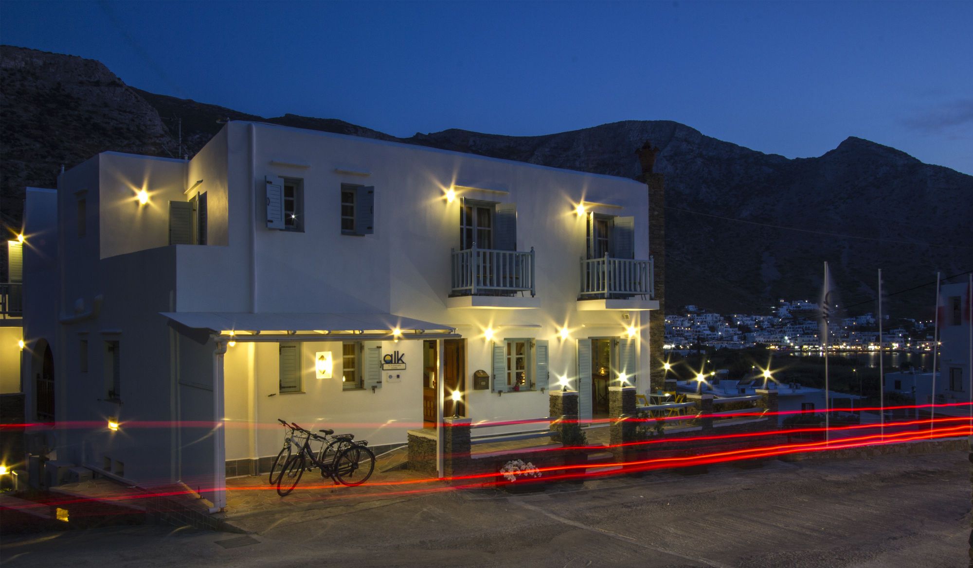 Un edificio de dos pisos con balcones, una bicicleta estacionada afuera y una vista de un pueblo al fondo.