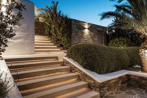 A set of outdoor stairs leading to a stone wall, surrounded by greenery and palm trees.