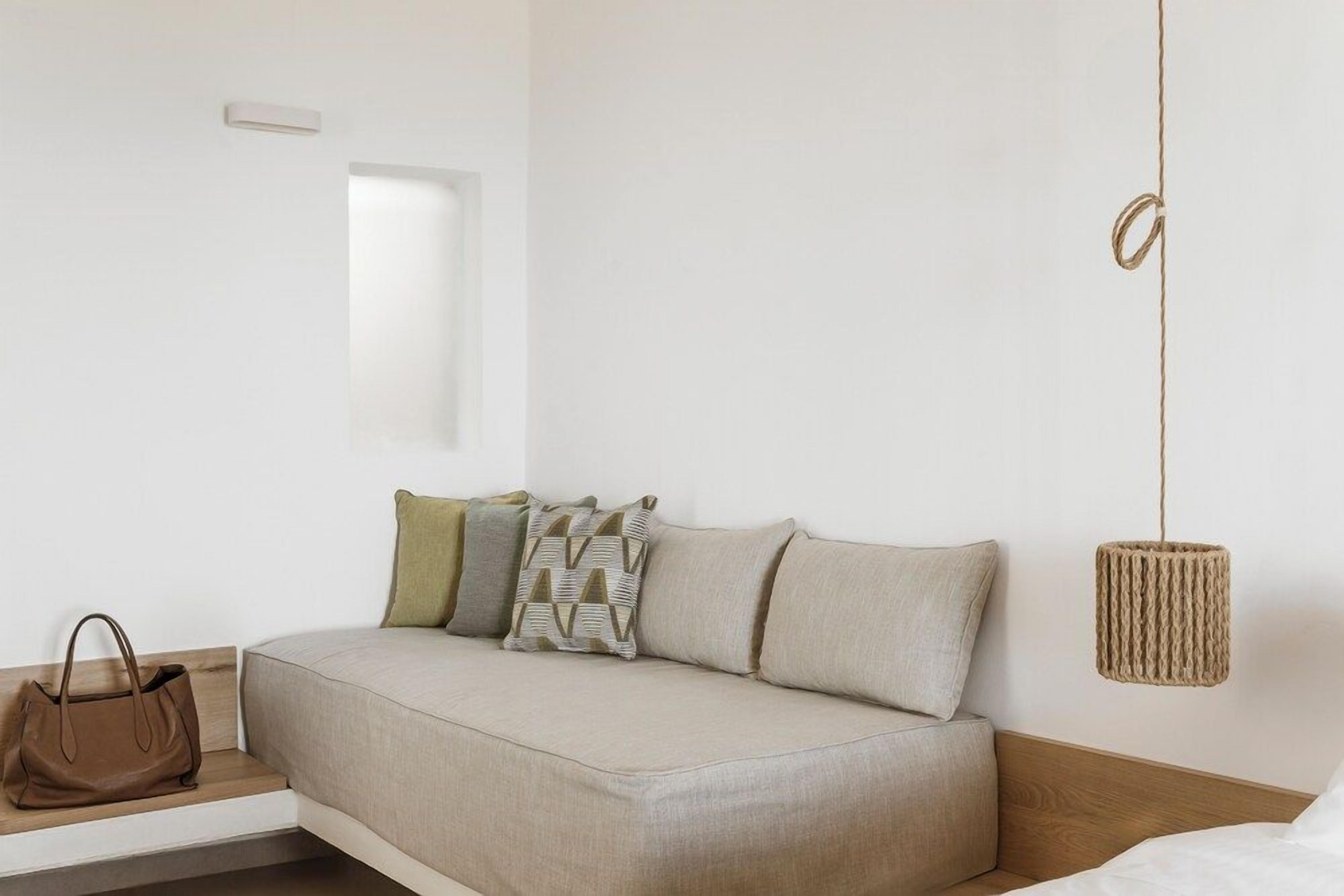 A neutral-colored sofa with cushions, a hanging woven light fixture, and a brown handbag on a wooden bench.