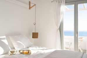 Un dormitorio con cama, lámpara colgante, bandeja de desayuno y vista al mar a través de una ventana.