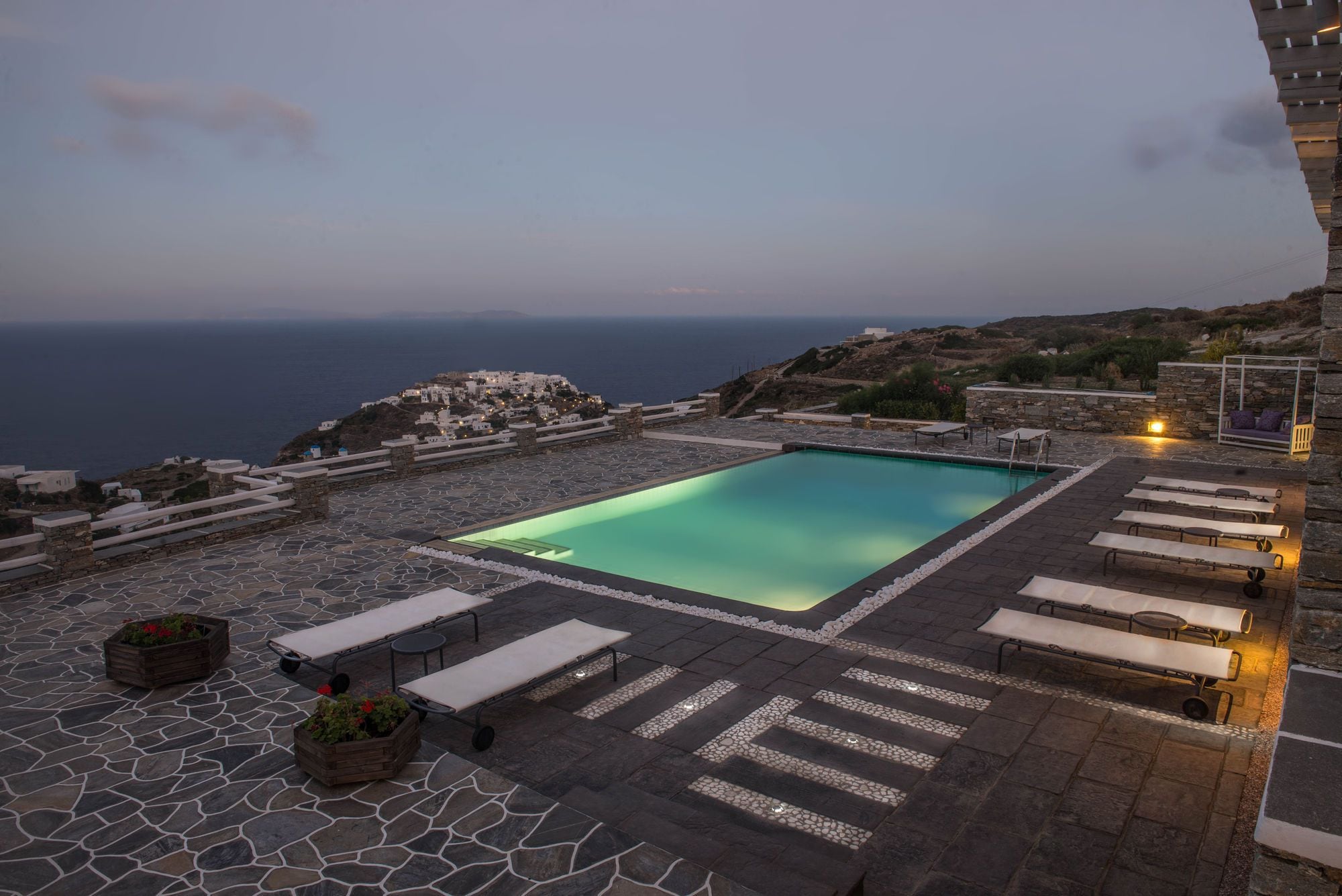 Une piscine sur le toit offrant une vue dégagée sur la mer et une terrasse en pierre avec des chaises longues.