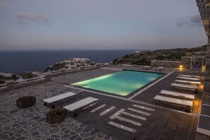 Una piscina en la azotea con vistas despejadas al mar y una terraza de piedra con sillones de descanso.