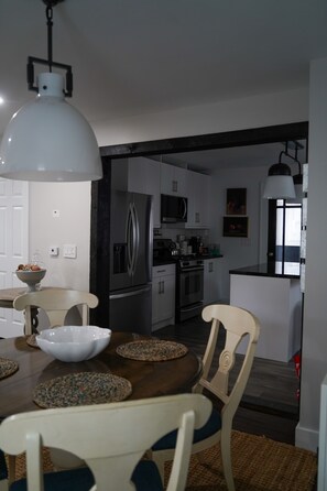 A modern kitchen with stainless steel appliances, a dining area with a wooden table and chairs, and a pendant light above the table. - Serene 4-bedroom house with central AC and heating in charming Norwalk (Norwalk)