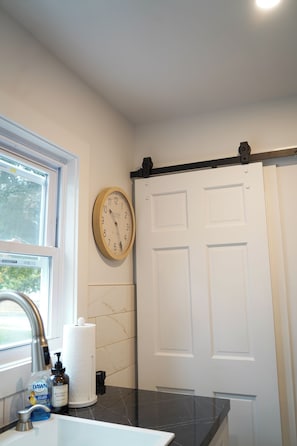 A bathroom with a sink, a clock, a towel dispenser, and a door. - Serene 4-bedroom house with central AC and heating in charming Norwalk (Norwalk)
