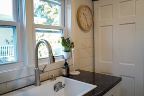 A kitchen with a stainless steel sink, a potted plant, a wall clock, and a door. - Serene 4-bedroom house with central AC and heating in charming Norwalk (Norwalk)