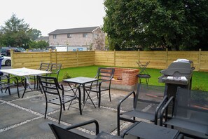 An outdoor patio area with a barbecue grill, tables, and chairs.