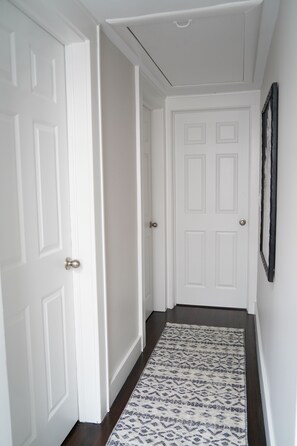 A hallway with white doors, a patterned rug, and a dark wooden floor.