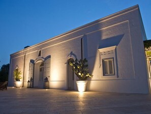 A building with a flat facade, arched windows, and a potted plant in the foreground. - Masseria Don Luigi (Fasano)