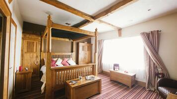 A room with a four-poster bed, a wooden cabinet, a small table, and a window with curtains.