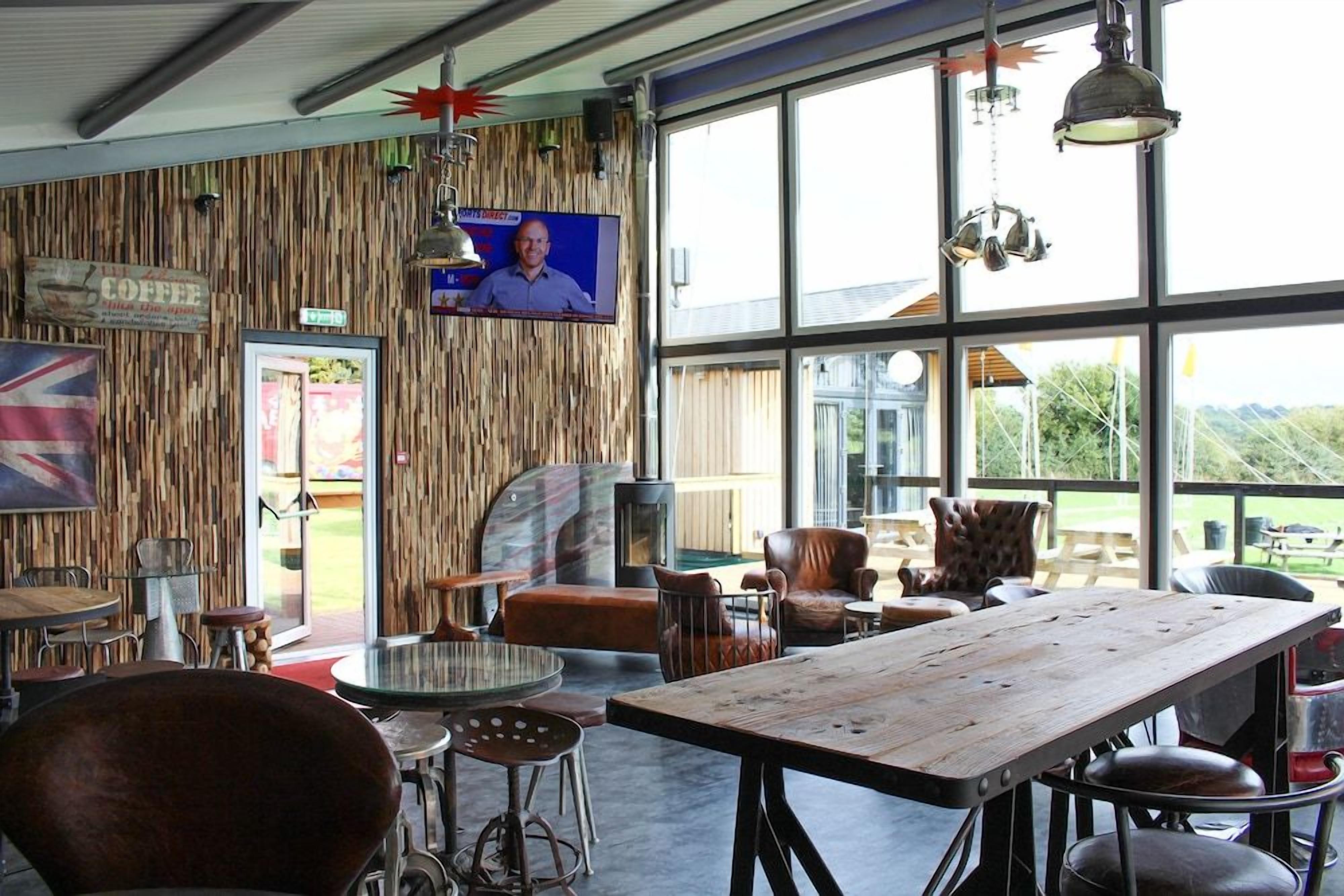 A rustic interior with a wooden wall, a television screen, and large windows.
