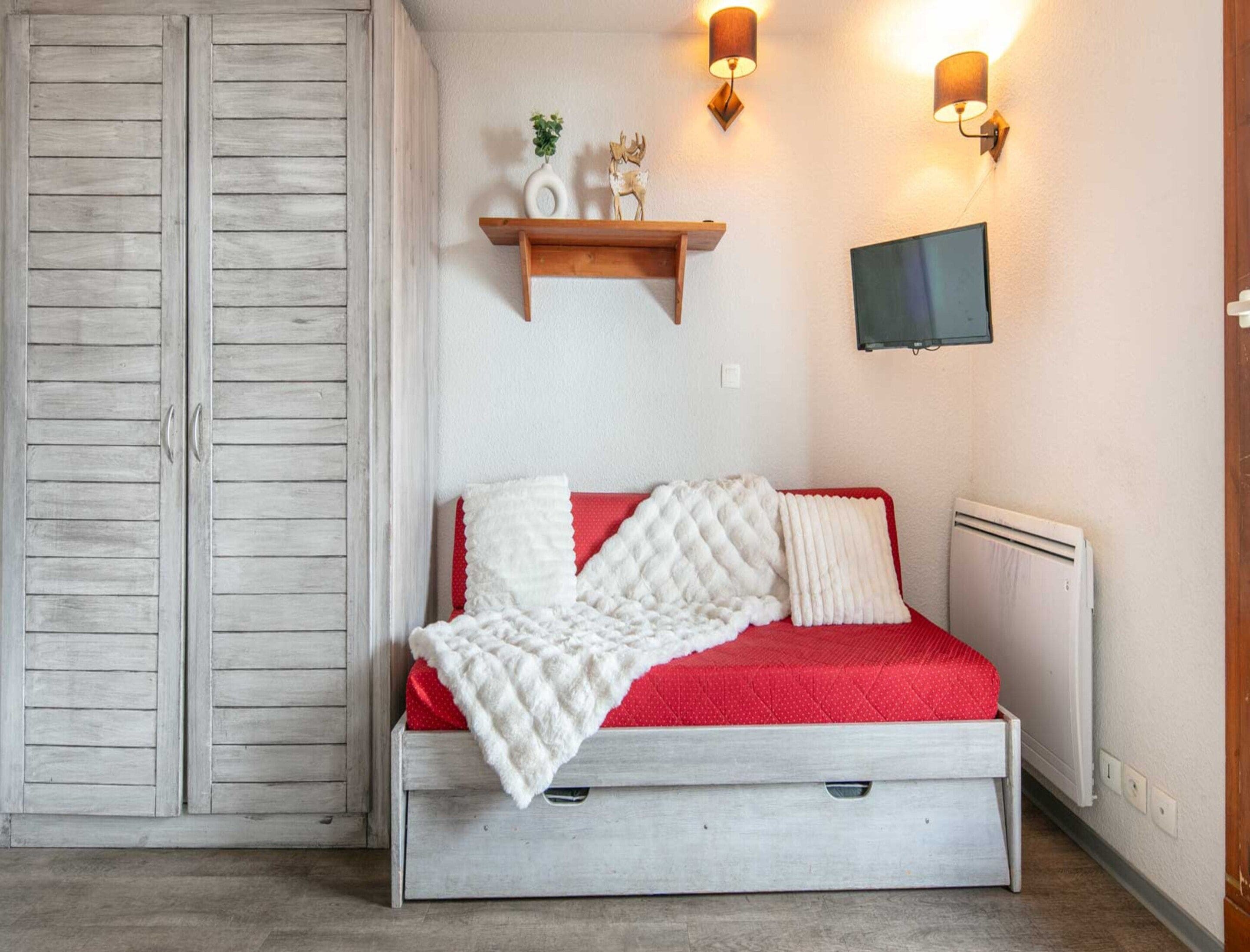 Une chambre à coucher comprenant un lit, une armoire, une étagère avec des objets décoratifs et des lampes fixées au mur.