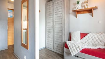 A bedroom with a bed, a wardrobe, a mirror, a shelf with decorative items, and a door leading to another room.
