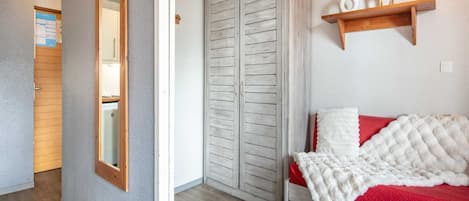 A bedroom with a bed, a wardrobe, a mirror, a shelf with decorative items, and a door leading to another room.