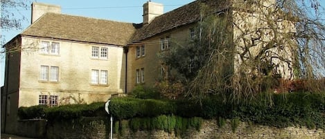 A two-story stone building with a traditional design, featuring a stone wall and a small garden area.