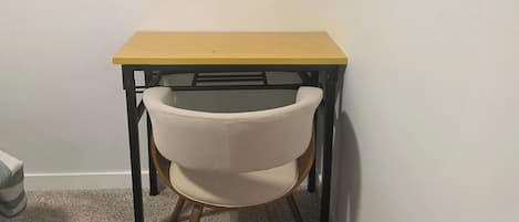 Habitación de esquina con una pequeña mesa de madera y una sola silla.