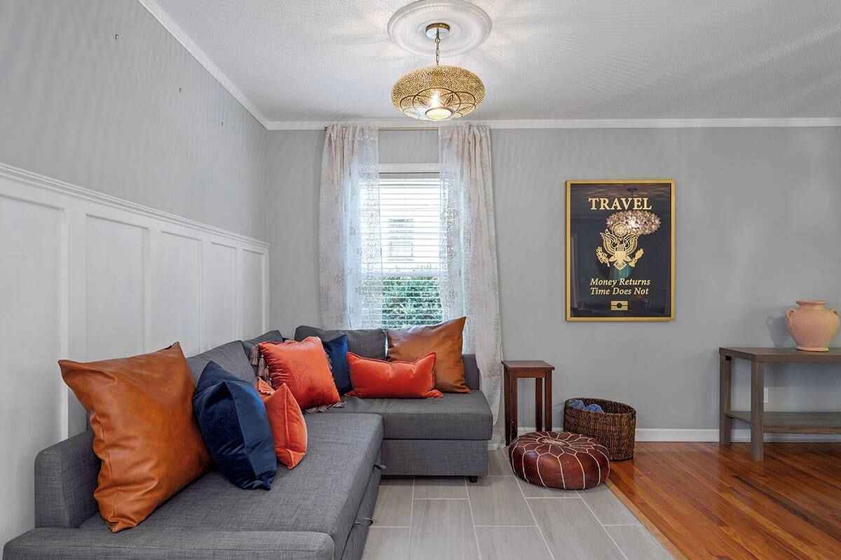 A modern living room with a grey sectional sofa, decorative pillows, a woven floor lamp, a framed travel poster, and a small side table.