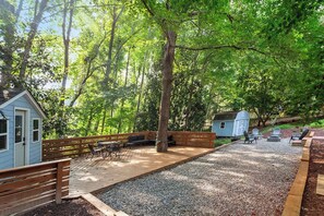 A deck with outdoor seating, a small shed, and a wooden fence in a wooded area. - Moroccan Retreat - Fire Pit & Private Yard (Raleigh)