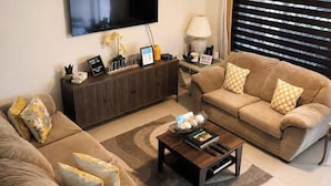 Una sala de estar con una televisión de pantalla plana, un conjunto de sofás, una mesa de centro y un armario.
