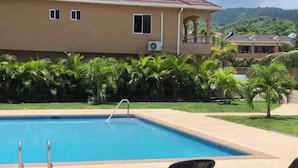 Una piscina con sillas de descanso, un edificio con balcón y palmeras.