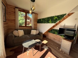 A cozy living room with a sofa, a small table, a TV, and a staircase with a green wall. - Demi chalet avec vue sur les pistes (Dévoluy)