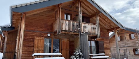 Una cabaña de madera con balcón, bancos cubiertos de nieve y un pequeño árbol.