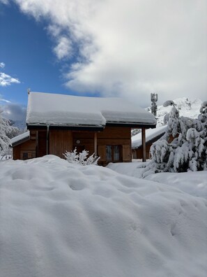 A wooden cabin with a snow-covered roof, surrounded by snow-covered trees and a mountainous backdrop. - Demi chalet avec vue sur les pistes (Dévoluy)