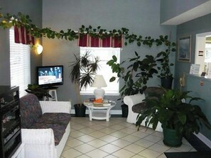 A living room with a television, a sofa, a coffee table, and several potted plants. - Key West Inn Cookeville (Cookeville)