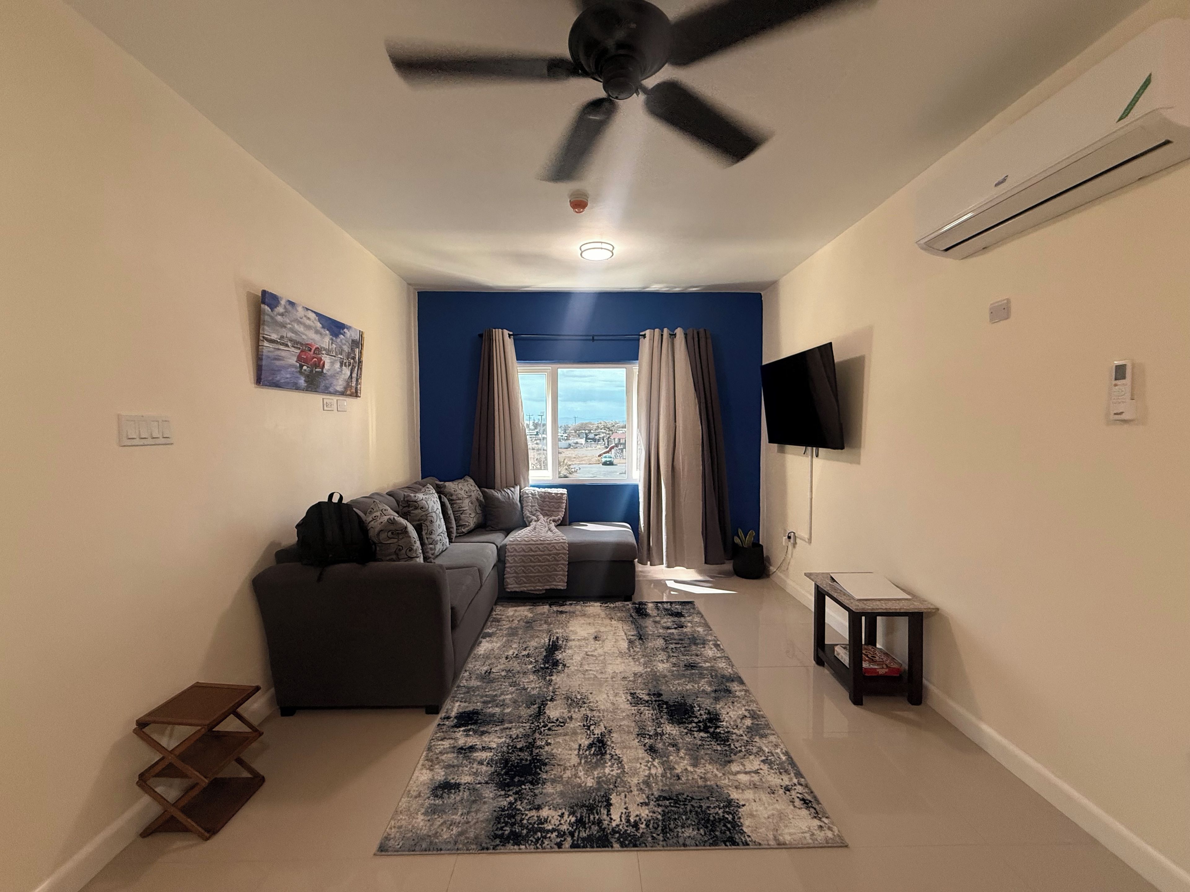 Una sala de estar con sofá, televisor, ventilador de techo y una ventana con cortinas.