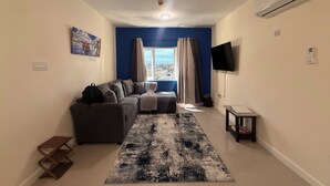 Una sala de estar con sofá, televisor, ventilador de techo y una ventana con cortinas.