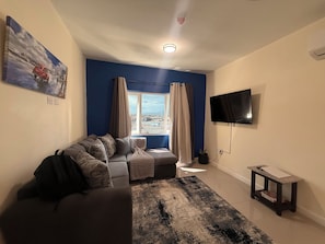 Un salon avec un canapé, un téléviseur, une fenêtre avec des rideaux et une vue sur l’extérieur.