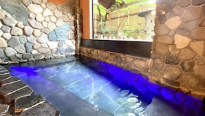 A stone-walled hot tub area with a view of a garden through a window. - Kinosaki Tenboen (Toyooka)