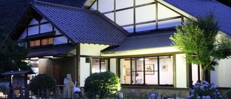 Une maison traditionnelle japonaise, dotée d’un toit en pente, de grandes fenêtres et d’un jardin clos.