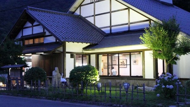 A traditional Japanese house with a sloped roof, large windows, and a fenced garden. - Kinosaki Tenboen (Toyooka)